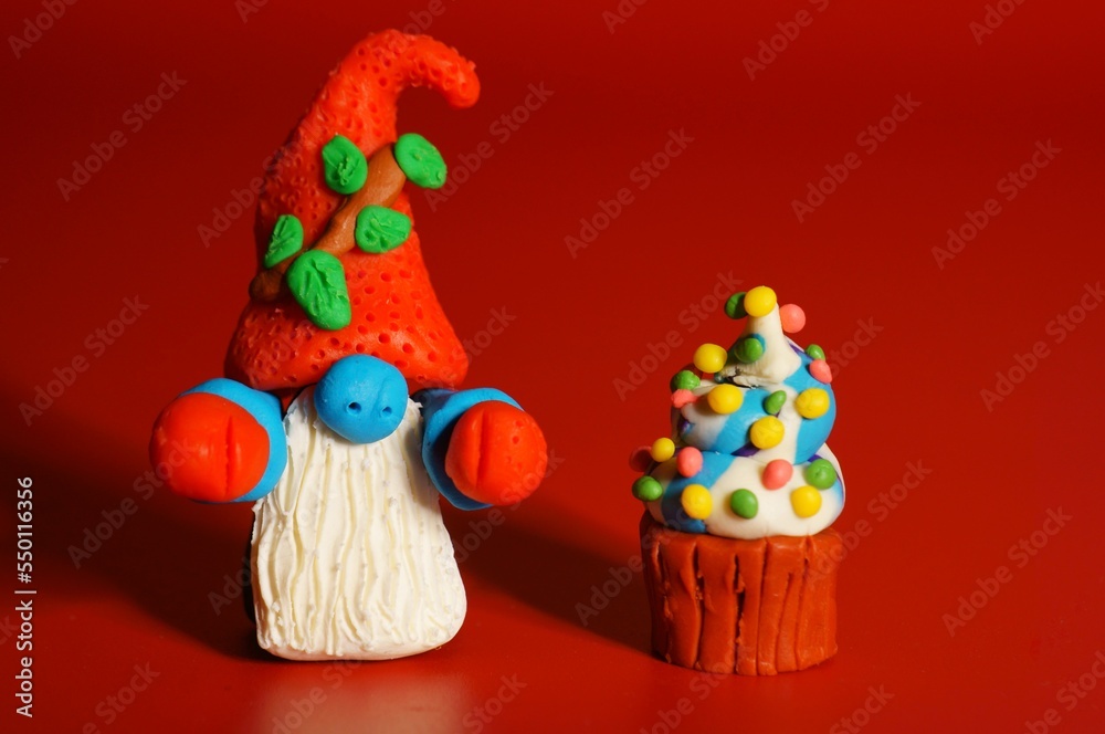 A toy gnome with a cupcake on a red background. New Year and Christmas. Fabulous scenery.