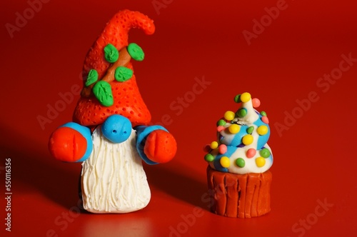 A toy gnome with a cupcake on a red background. New Year and Christmas. Fabulous scenery.