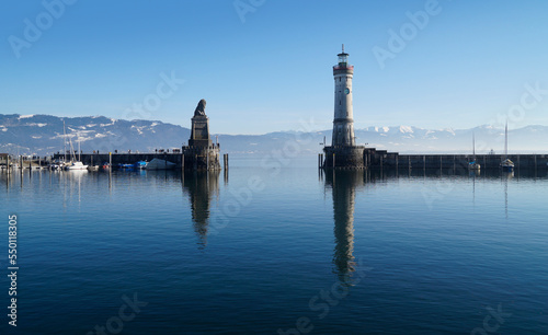 harbour of Lindau island on tranquil lake Constance or lake Bodensee with the Alps in the background on a fine winter evening with the scenic sky and white clouds reflected in the water (Germany)