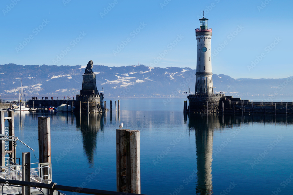 harbour of Lindau on tranquil wintery lake Constance or lake Bodensee with the Alps in the background on a fine winter evening with the scenic sky and white clouds reflected in the water (Germany)