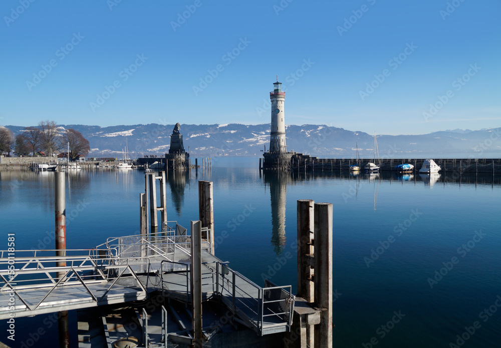 harbour of Lindau on tranquil wintery lake Constance or lake Bodensee with the Alps in the background on a fine winter evening with the scenic sky and white clouds reflected in the water (Germany)