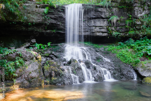 Beautiful waterfall during spring with silver colored water, cascading down the cliff covered by green plants