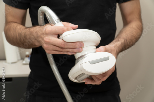 Cloce up male hands  holds an apparatus for LPG massage of a roller vacuum for weight loss and cellulite correction against the background of an office and a monitor for turning on the LPG apparatus photo