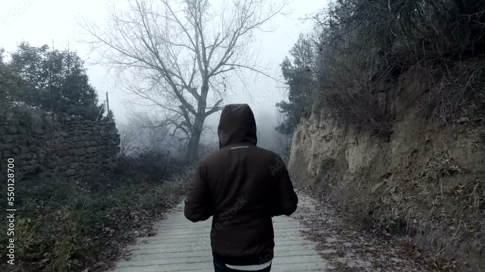 Hombre joven andando en paisaje de invierno con niebla. Camino entre arboles secos y vegetacion.