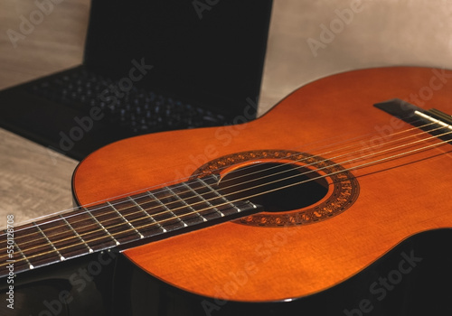 Classic acoustic orange guitar with a black laptop on a wood textured table. Online instruction