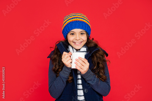 portrait of child with coffee cup. drinking cocoa and milk. glad kid in puffer waistcoat and hat