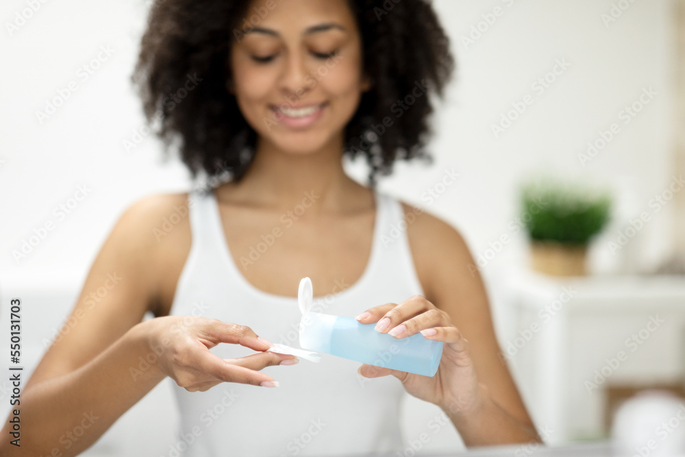 A black woman applies micellar water to a cotton swab in the bathroom at home. A black woman applies micellar water to a cotton swab in the bathroom at home.