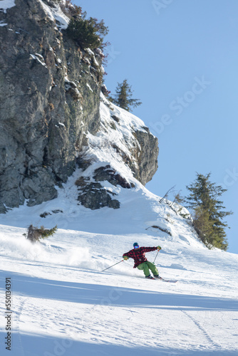 freeride skier skiing downhill during sunny day in high mountains