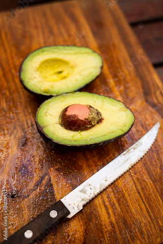 avocado cut in half next to a knife on a cutting wood