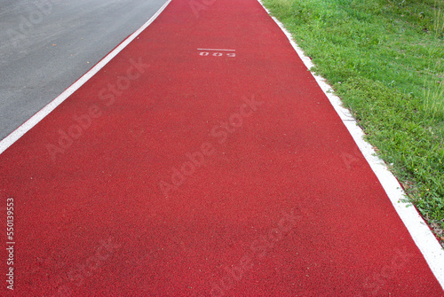 Red running track in the park. Jogging red track in the park next to the asphalt 