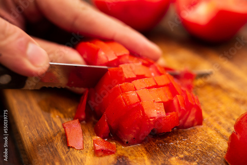 person cutting tomatoes into cubes on a piece of wood