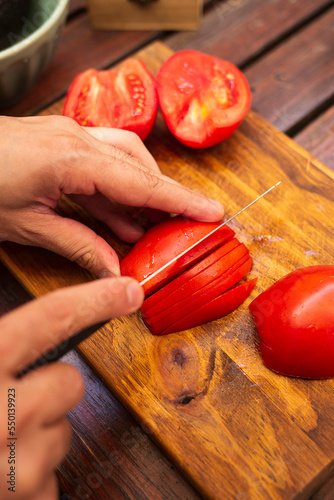person cutting tomatoes in julienne on a wood