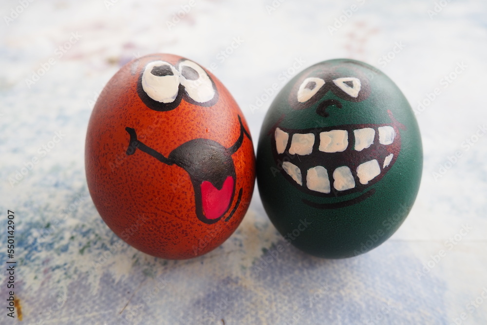 Easter eggs dyed green and brown with painted laughing faces. Funny grimaces with eyes, tongue and big white teeth. Scary face for Halloween. Emoticon for Easter. Light abstract background.