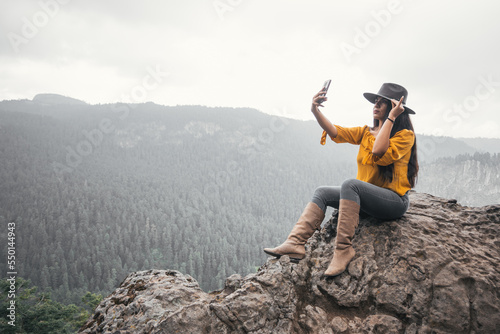 Young woman taking self portrait with her cell phone in a forest landscape