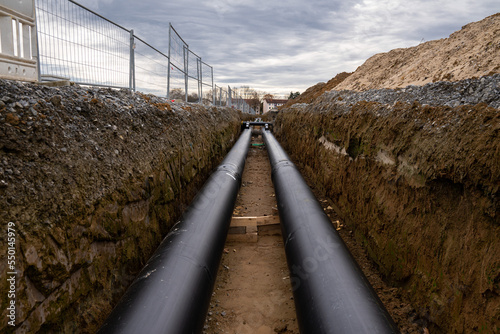Two large metal pipes with a plastic sheath laid in a trench.