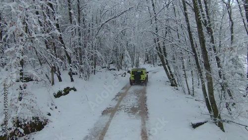 MARCH 2022, LJUBLJANA, SLOVENIA: AERIAL: Beautiful winter drive with Jimny Suzuki 4x4 car through snowy forest. Mini 4-wheel SUV vehicle moving through woodland along snow-covered road on cloudy day. photo