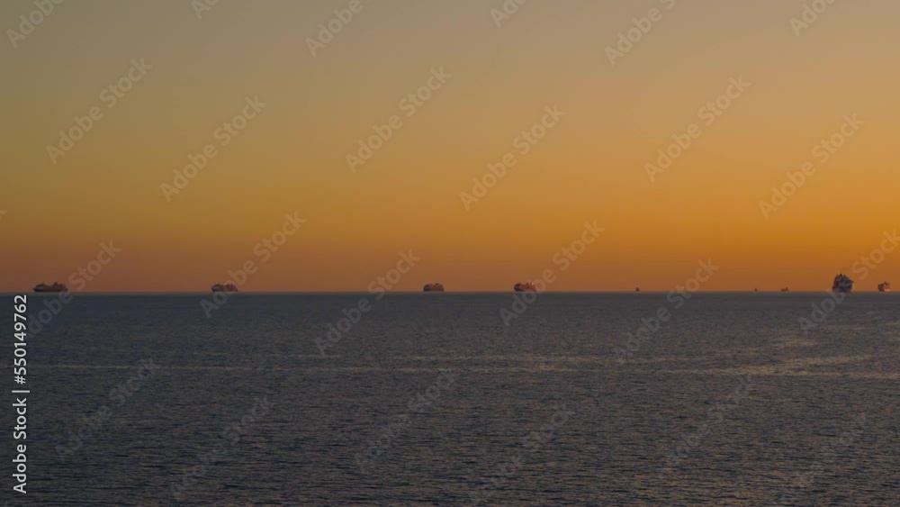 Sea in twilight of sunset. On horizon, silhouettes of anchored ships on distant roadstead are barely noticeable Sea in twilight of sunset. On horizon, silhouettes of anchored ships on distant roadstead are barely noticeable