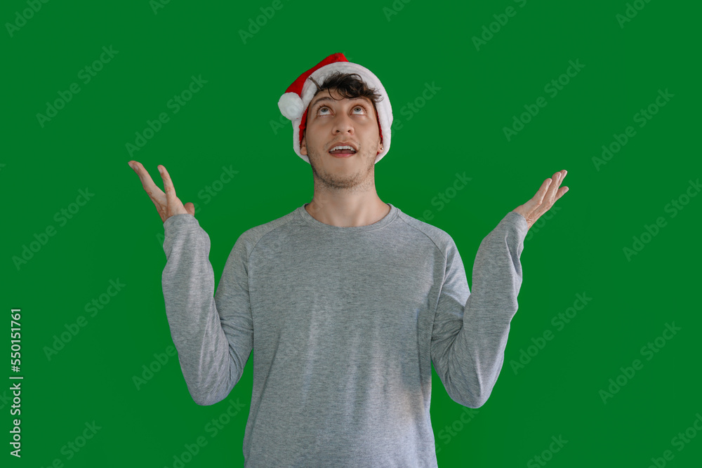 An astonished young Latino man looking up with Christmas hat and open arms upward. An astonished young Latino man looking up with Christmas hat and open arms upward.