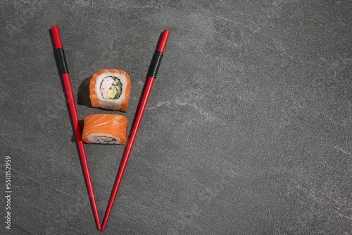 Sushi rolls with salmon, avocado and cucumber with red chopsticks on a black stone (slate) background.