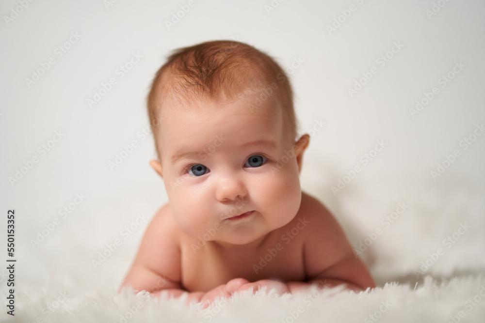 portrait of an infant with serious emotion lying on his belly against a white background portrait of an infant with serious emotion lying on his belly against a white background