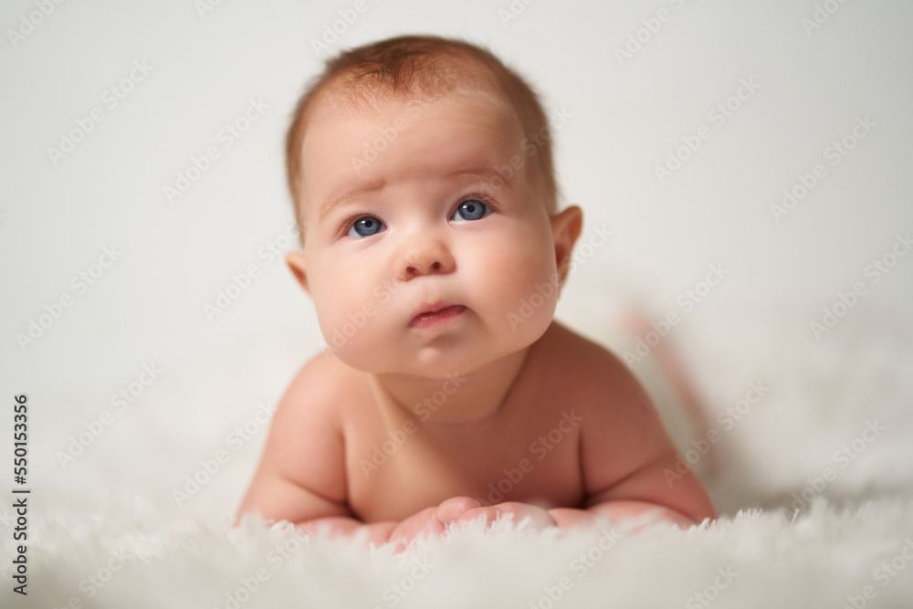 portrait of an infant with serious emotion lying on his belly against a white background portrait of an infant with serious emotion lying on his belly against a white background