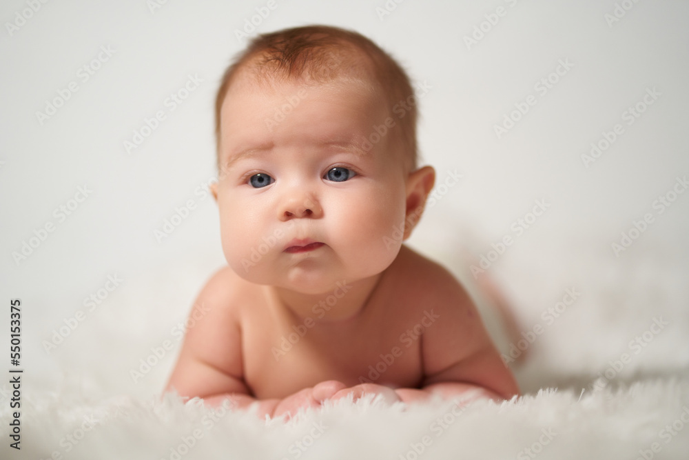 portrait of an infant with serious emotion lying on his belly against a white background portrait of an infant with serious emotion lying on his belly against a white background