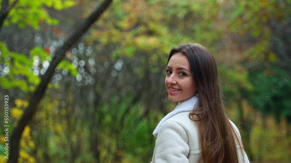 Smiling brunette in light warm jacket walking in the nature. Girl taking a stroll in the park in autumn. Blurred backdrop. Smiling brunette in light warm jacket walking in the nature. Girl taking a stroll in the park in autumn. Blurred backdrop.