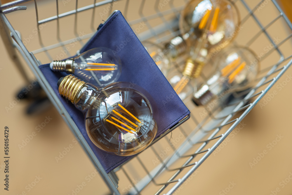 Consumption and payment for energy consumption. Purchase of electricity.lot of electric lamps in a shopping cart.Light bulbs in a supermarket trolley on a beige background.Crisis in the energy sector.