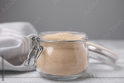 Granulated yeast in glass jar on white wooden table, closeup