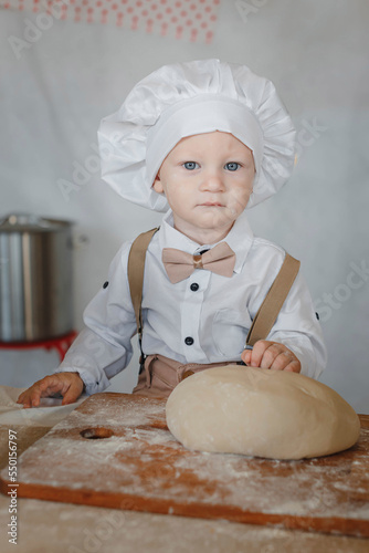  little boy in a chef's cap and apron in the kitchen with a dough