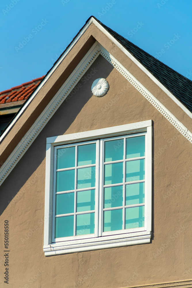 Double gable roof with brown stucco exterior with red brick roof tiles and window with white accent color