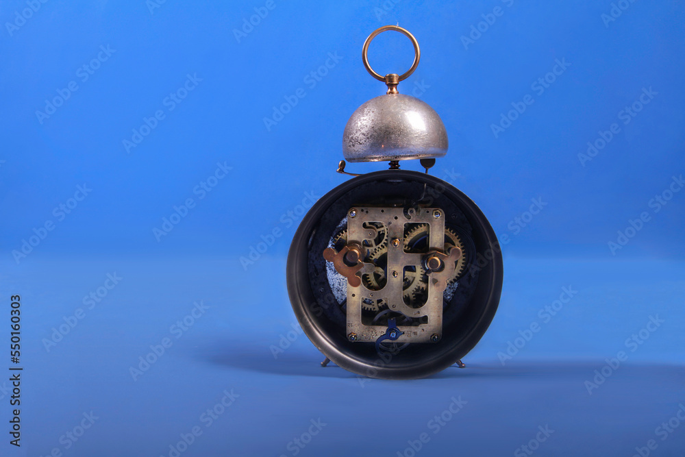 Inside retro oldfashioned vintage mechanical silver alarm clock with gold gear elements on blur blue background