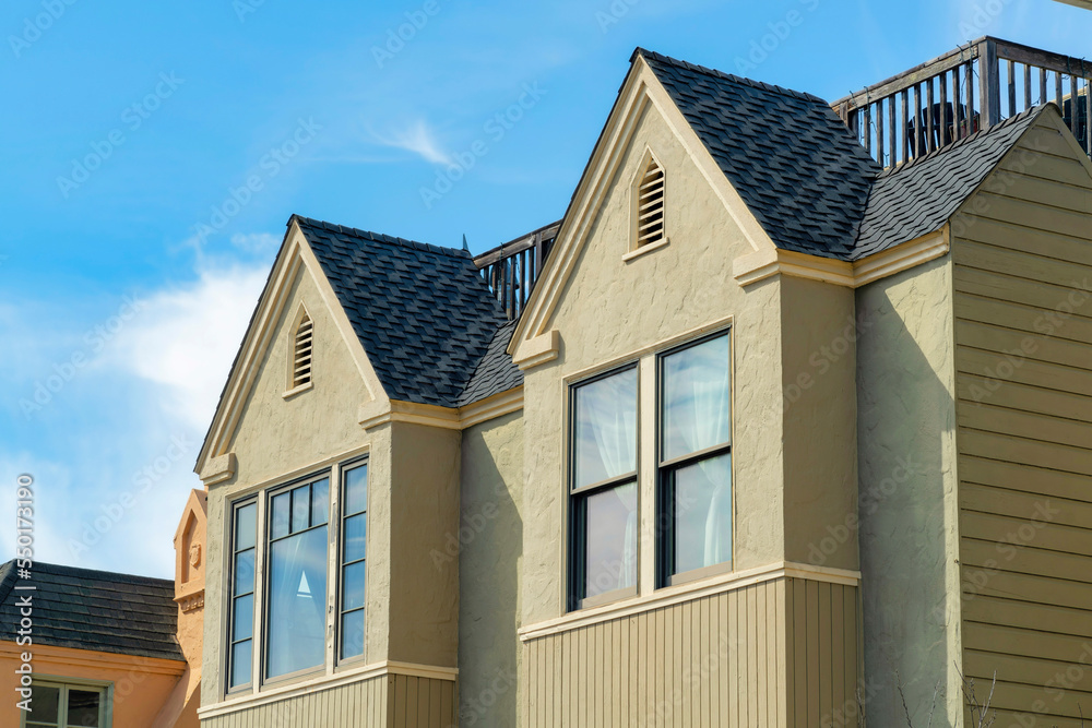 Beige or brown house facade with windows and double gable roofs in midday sun in the city neighborhood