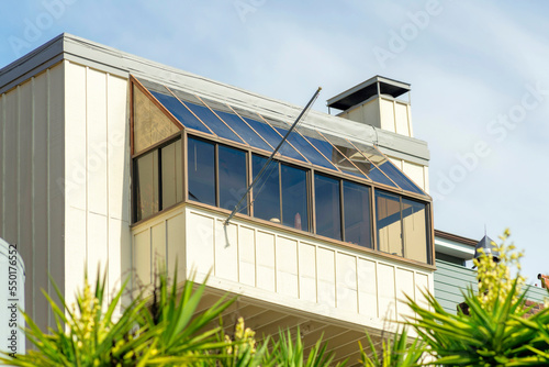 Bay style window or sun roof with vertical wood pannels beige and chimney and front yard foliage plants or trees and blue sky