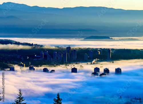 High-rise buildings substantially obscured by dense BC cloud inversion with mountains in silhouette in background. photo