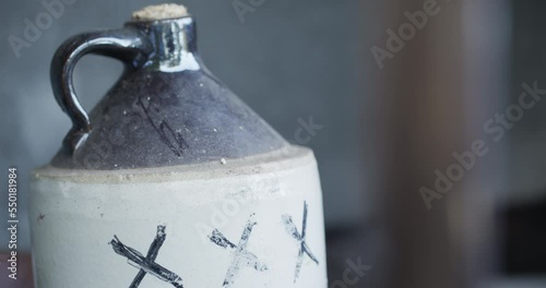 A corked ceramic jug of moonshine liquor marked with the letters 'XXX' sits with the background out of focus. photo