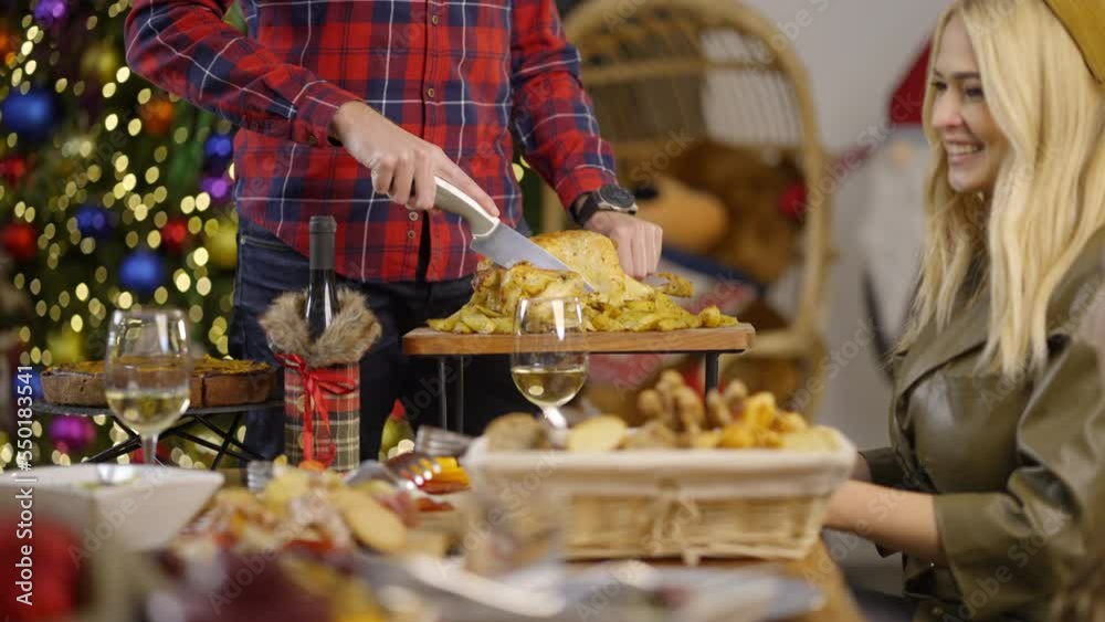 Man�s hands cutting a chicken with a knife, while woman is talking with family on Christmas dinner. Slow motion. Man�s hands cutting a chicken with a knife, while woman is talking with family on Christmas dinner. Slow motion.