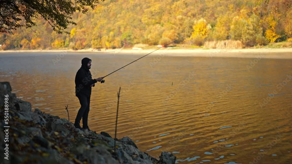 Young man in black hoodie and jacket throwing a spinning rod into the lake.