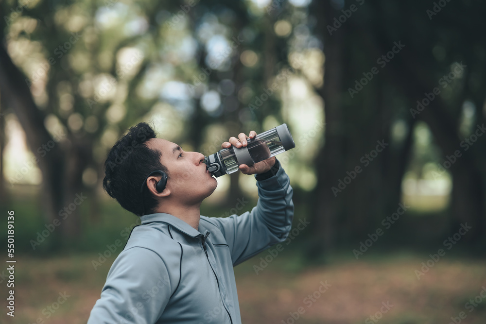 Young sport man drink water after jogging, running in the park. Sport thirsty and resting after exercise.. Young sport man drink water after jogging, running in the park. Sport thirsty and resting after exercise..