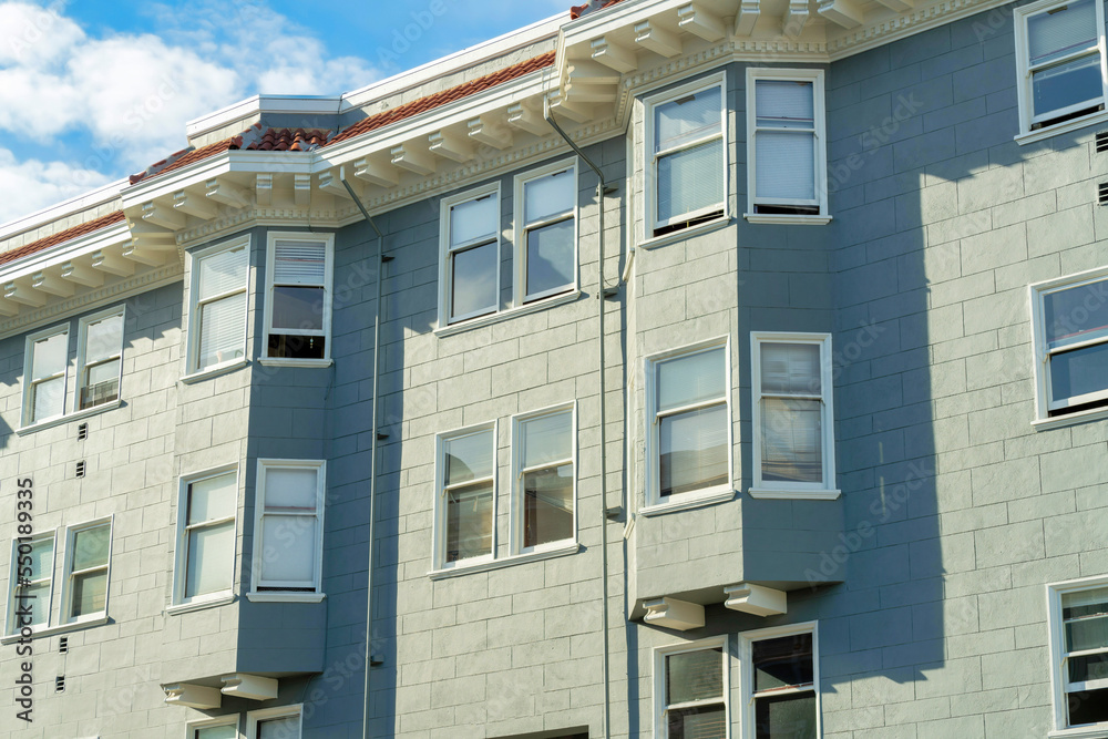 Building facade with gray and green stucco paint and a great many windows with blue and cloudy sky background Building facade with gray and green stucco paint and a great many windows with blue and cloudy sky background