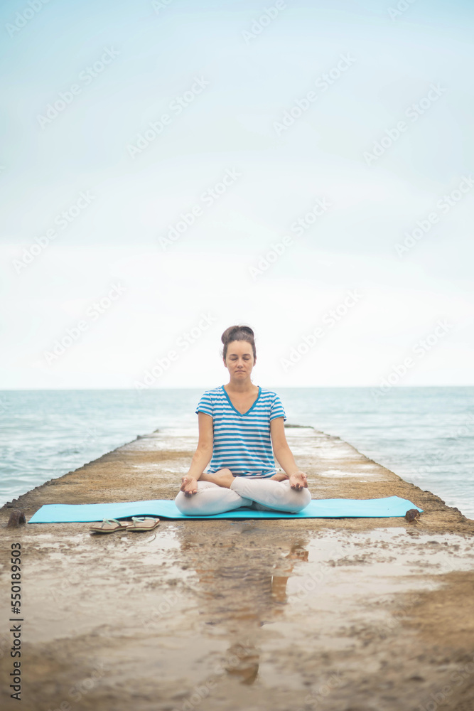 Woman yoga instructor sitting in lotus posture hands mudra admiring sea coastline landscape Woman yoga instructor sitting in lotus posture hands mudra admiring sea coastline landscape