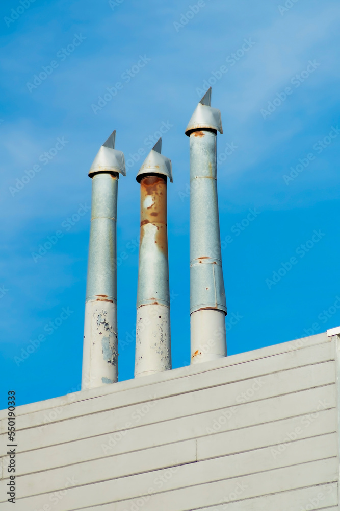 Gray metal chimney pipes with some rust and wooden slatted building exterior facade with blue sky background Gray metal chimney pipes with some rust and wooden slatted building exterior facade with blue sky background