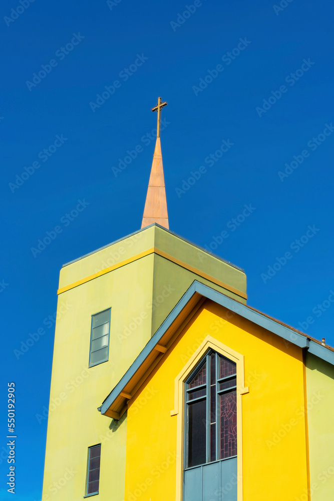 Colorful church steeple with orange and green stucco and rooftop cross with dark blue sky background no clouds