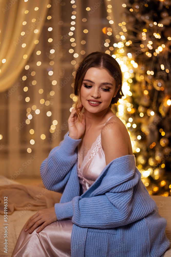 beautiful young girl in a nightgown and a sweater in a decorated New Year's bedroom interior beautiful young girl in a nightgown and a sweater in a decorated New Year's bedroom interior