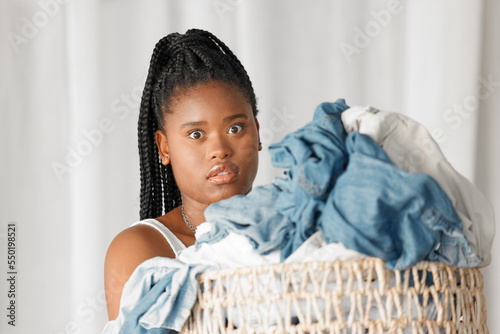 Portrait, laundry and wow with a black woman cleaner carrying a basket of clothing for washing in her home. Cleaning, face and shock with a female housekeeper doing housework or chores with surprise photo