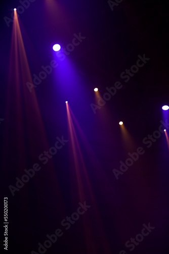 Purple beams of light from stage spotlights on a dark background.