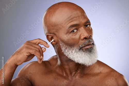 Black man, cleaning ear and cotton bud for hygiene, wellness and wax with face, portrait and purple studio background. Senior male with ears, cleaner and self care for earwax , remove and stick photo