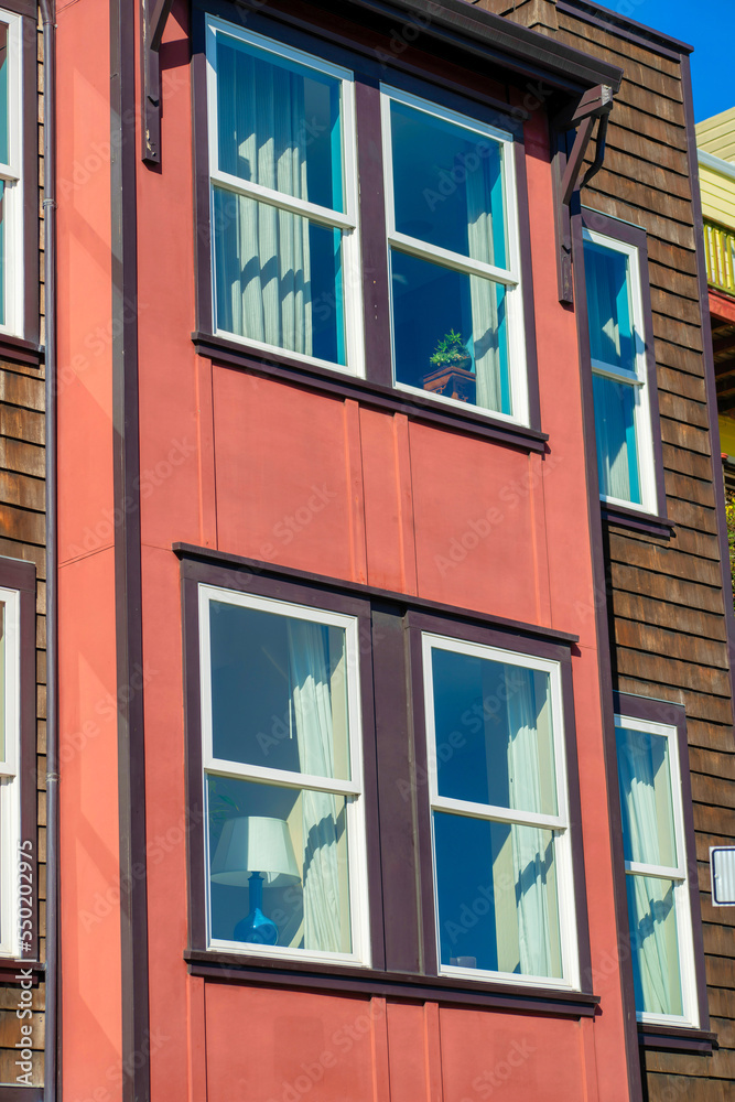 Red wooden house facade in bright midday sun with brown exterior paint and white accent color near windows