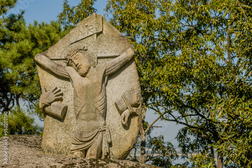 Stone carved figure representing Jesus Christ on cross at Catholic church nature park.