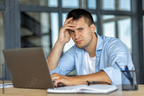 Depressed businessman sitting at the workplace in the office, received bad news in the email, thinks. Upset Caucasian entrepreneur having problems at work